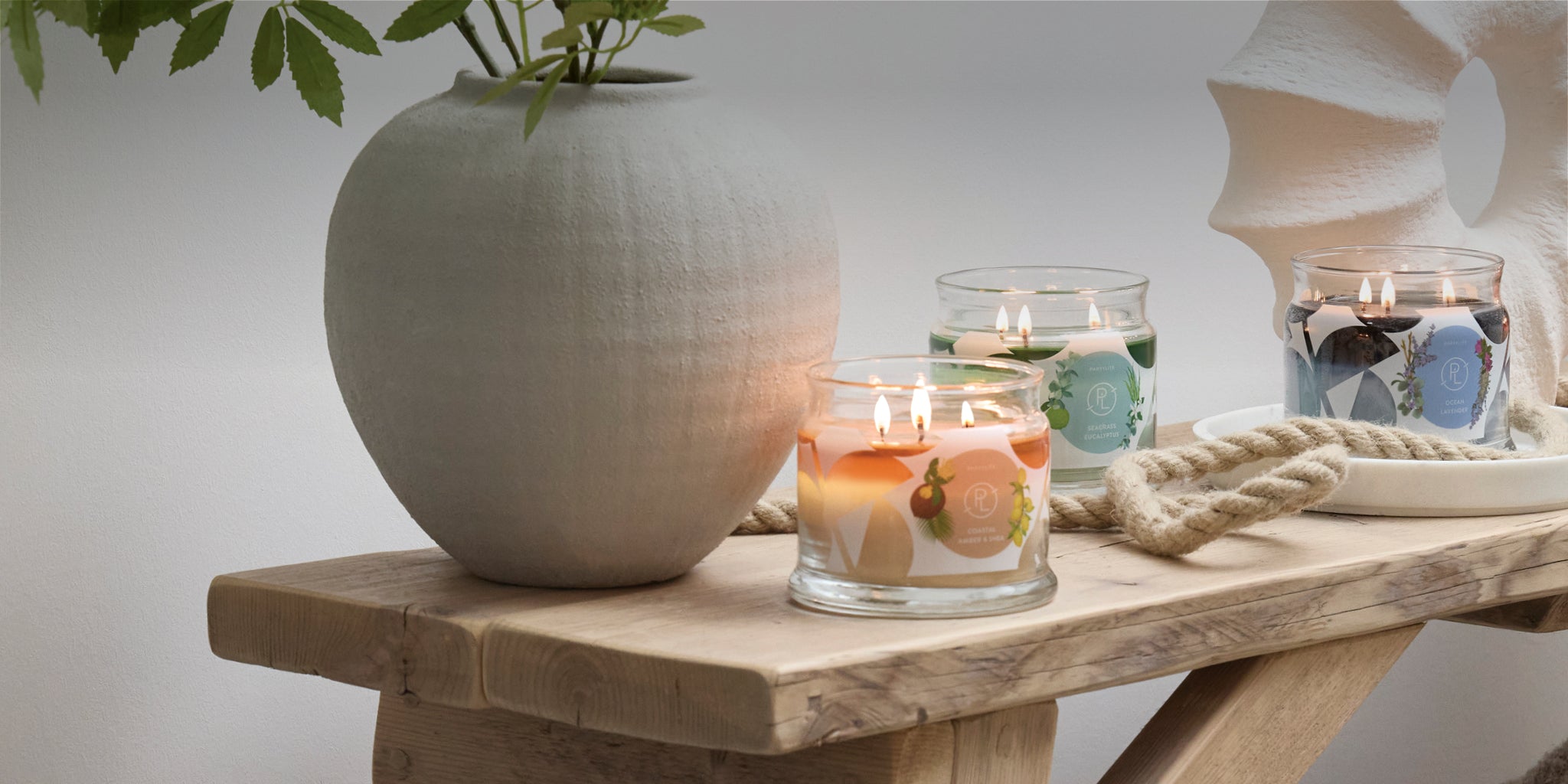 Three 3-wick jar candles with nautical decorations on a wooden table.