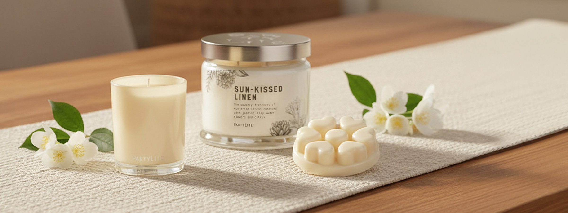 Sun-Kissed Linen 3-wick, melt and Escential Jar with white flowers on a wooden table with table runner