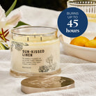 Sun-Kissed Linen 3-wick jar candle with a decorative lid on a white surface, with the burn time advised.