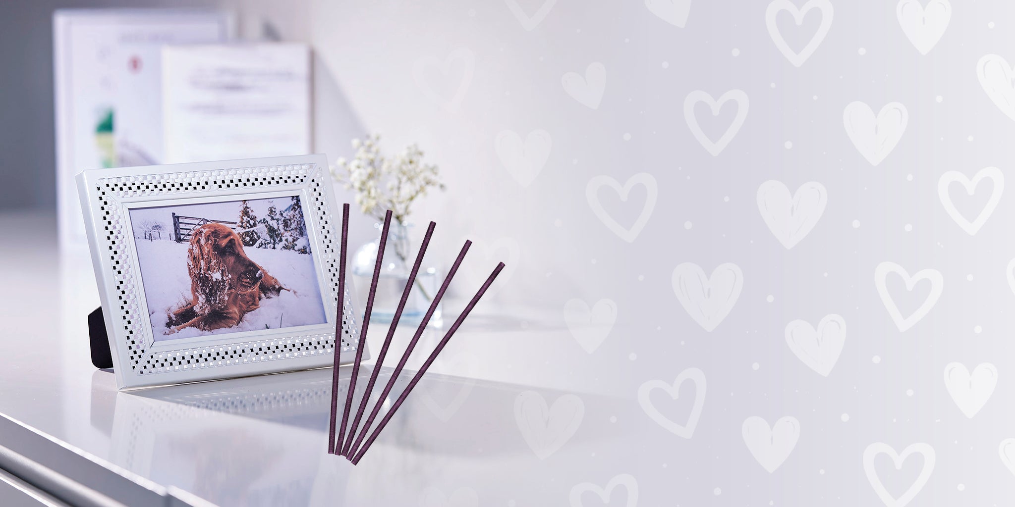 Small photo frame with a dog picture on a white surface with PartyLite fragrance sticks on a heart patterned background.