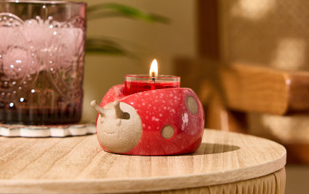 Loveable Ladybug Tealight Holder on a wooden table with a glass and a blurred chair in the background