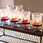 Set of four lit candle holders on a decorative stand with a blurred background