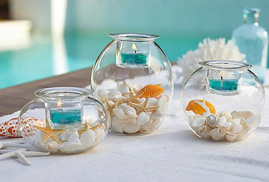 Clearly Creative Tealight Trio with lit tealights, decorative shells and pebbles on a white cloth. 