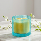 Dragonfruit Zest specialty jar candle green ribbed glass with yellow wax, shown on a light colored table with small white flowers.
