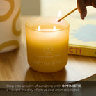 Yellow candle labeled 'Optimistic' being lit on a wooden surface with a blurred background.