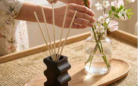 Curvy Black Tealight/SmartScents Holder with Smartscents on a wooden tray next to a vase of flowers being arranged