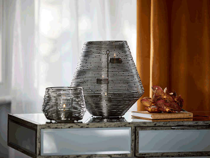 Spun Wire Votive Holder and Hurricane shown together with lit candles on a tab le with curtains in the background.