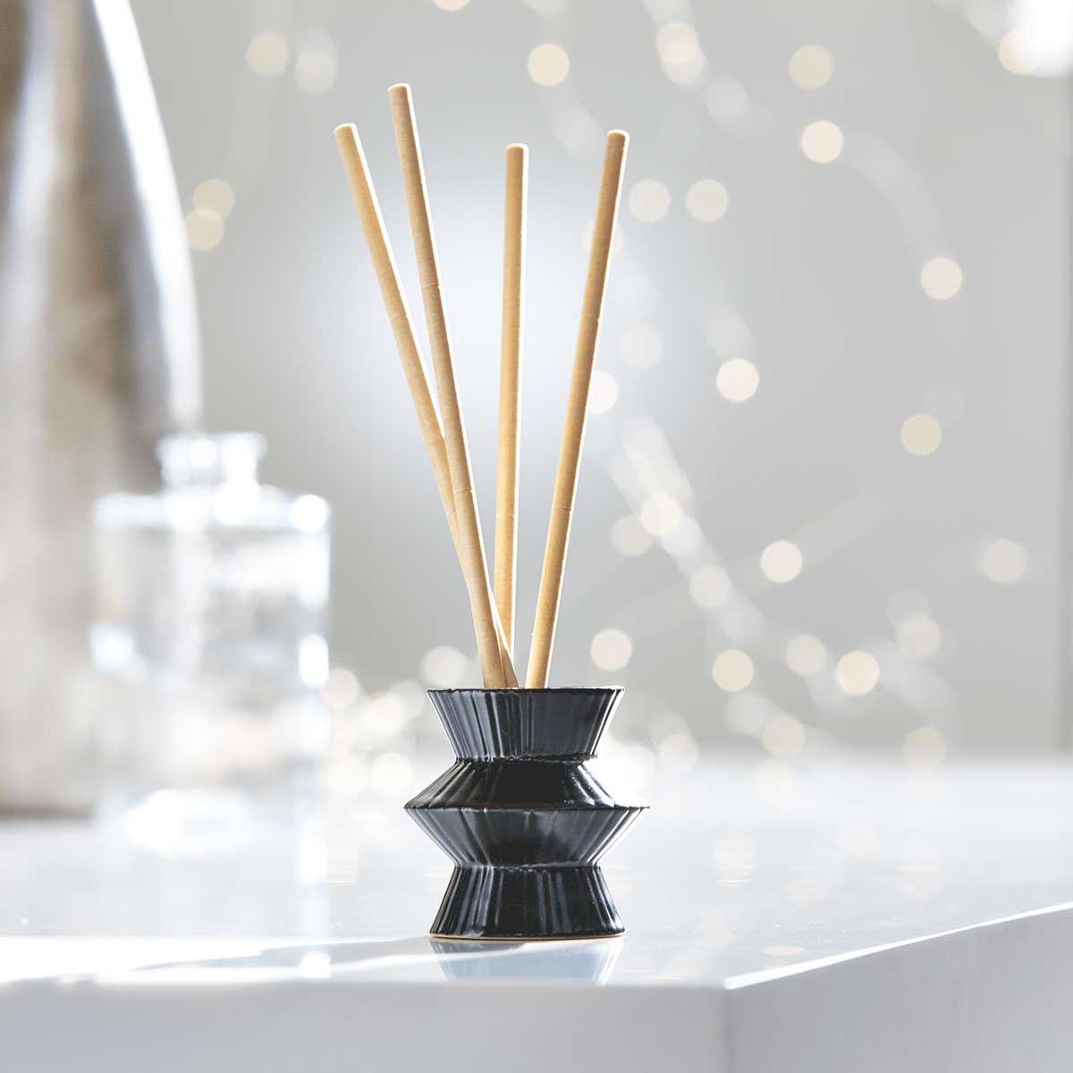 Black Pinstripes Fragrance Holder shown with fragrance sticks, against a blurred background.
