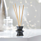 Black Pinstripes Fragrance Holder shown with fragrance sticks, against a blurred background.