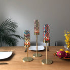 Tribal Chic Raised Tealight Holder Trio colorful pattern cup on a gold stand on a wooden dining table with plate settings.