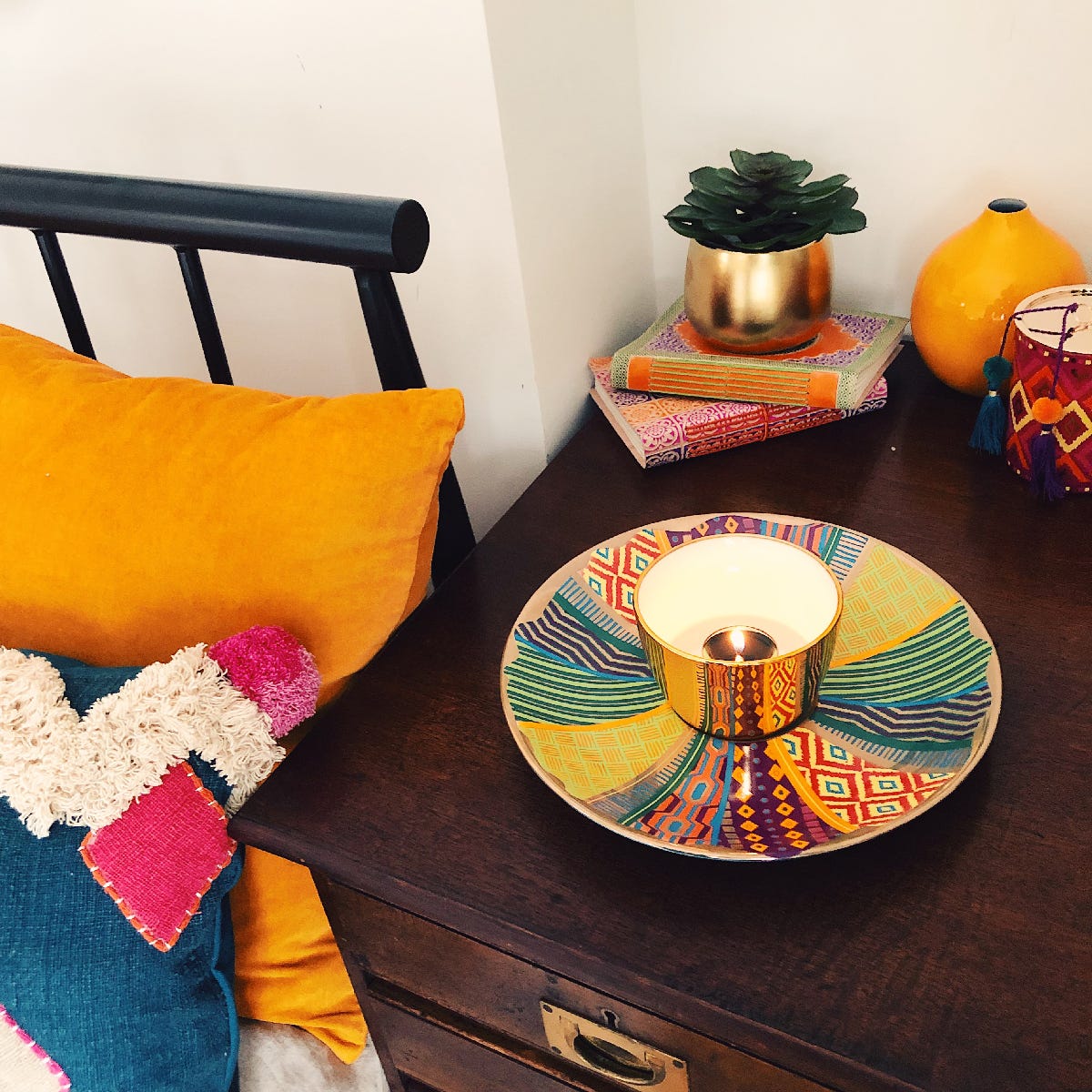 Tribal Chic Reflections Large Tealight Holder colorful pattern saucer with a holder in the middle, on  a dark wooden table with books in the background.