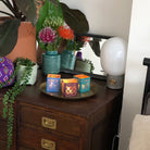 Tribal Chic Metal Tealight Candle Holder Trio on a bronze metal round tray on a dark wooden surface with a plants and vase of flowers next to them.