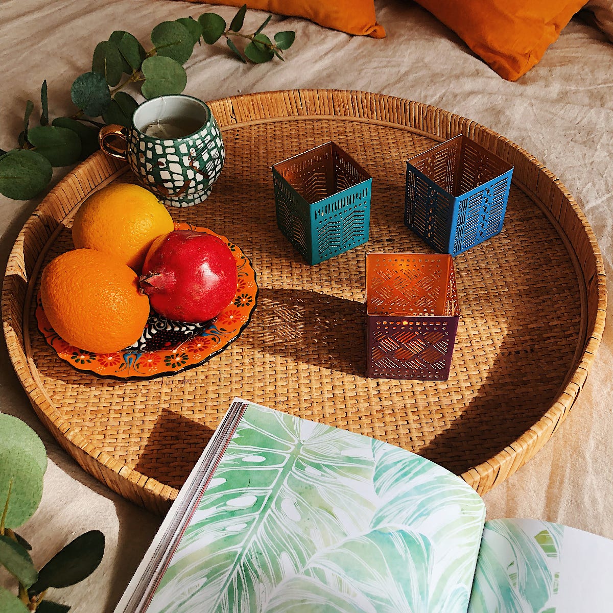 Tribal Chic Metal Tealight Candle Holder Trio, shown a wooven tray with a plate of fruits next to them.