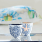 Sealife Tealight Holder Pair light colored holders with blue tree and a light colored star. shown on a reflective surface.