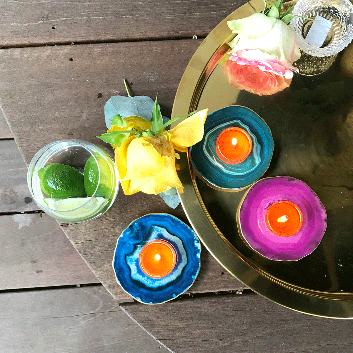 Faux Agate Tealight Holder Trio in blue, green and pink colors shown with lit tealighrts, with a yellow rose and a gold tray on a wooden table.