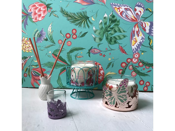 Pineapple shaped fragrance stick holder, various jar holders against colorful wallpaper of flowers and butterflies on a light surface.