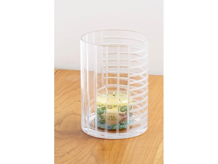Linear Lines Glass Hurricane Candle Holder shown with a lit 3-wick jar on a wooden surface with a light background.